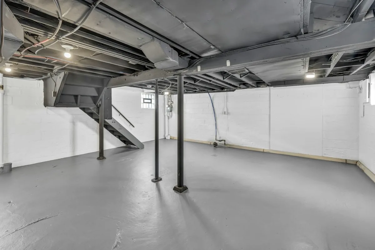 Unfinished basement with steel support posts and exposed floor joists of the kind that commonly houses an older heating oil tank
